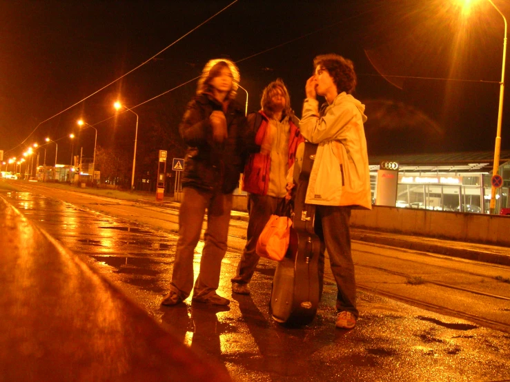 three people standing on wet road during the rain