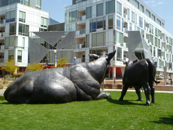 two sculptures sitting in the grass near tall buildings