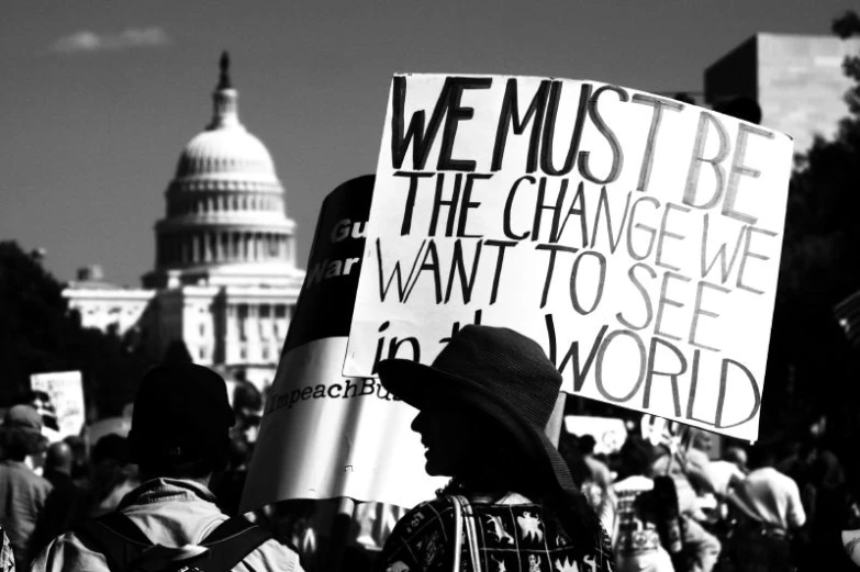 a man holding a sign that reads we must be the change we want to see in world