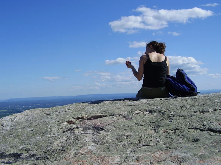 a woman sitting on top of a rock next to a backpack