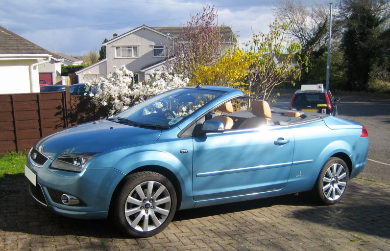 a blue convertible vehicle is parked on a driveway in front of two houses