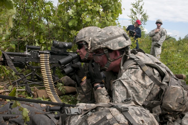 three men in camouflage look at each other while they prepare to fire a rifle