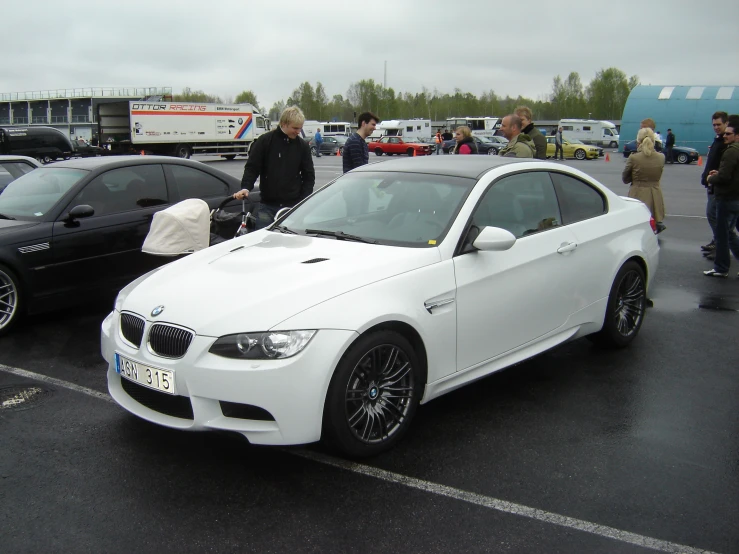 people standing around a white bmw car near other cars