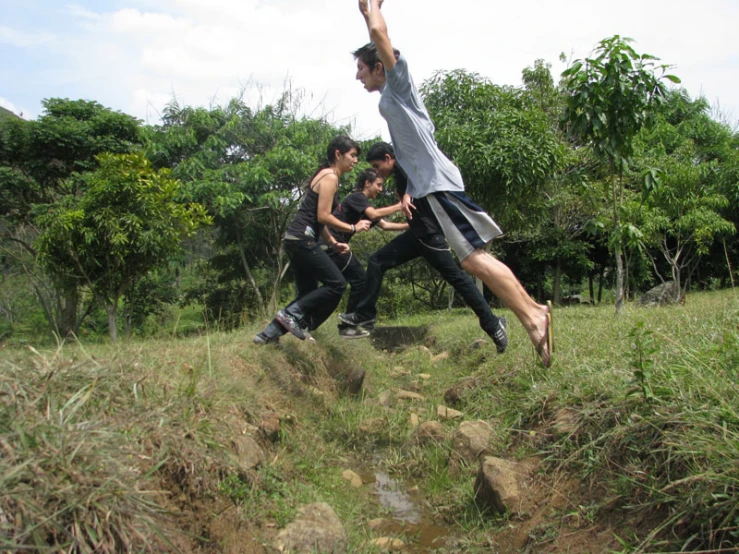 three boys playing frisbee on top of hill with trees behind them