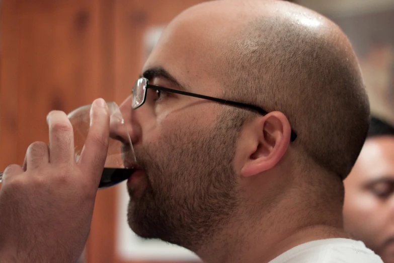a man with glasses drinks from a glass
