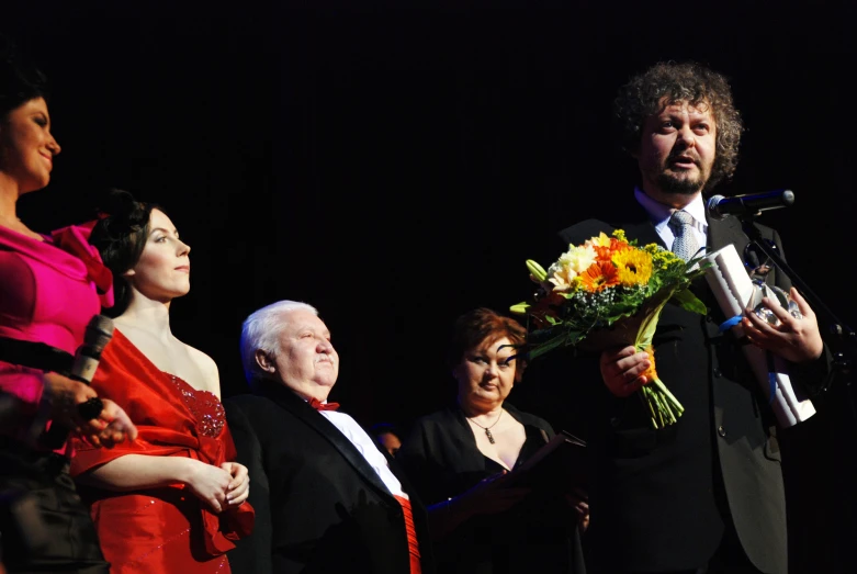 there are four people standing together with one holding flowers