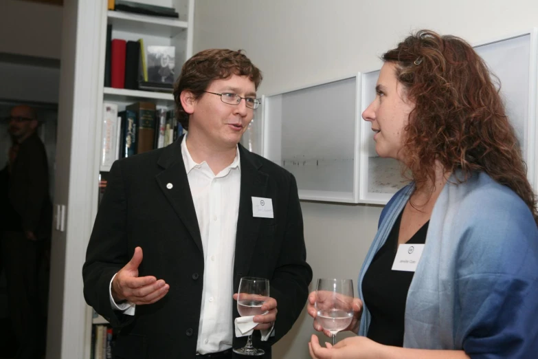 two people standing in a room talking and drinking wine