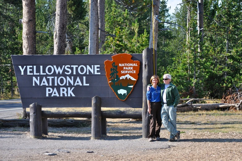 two people standing by a large sign at the yellowstone national park