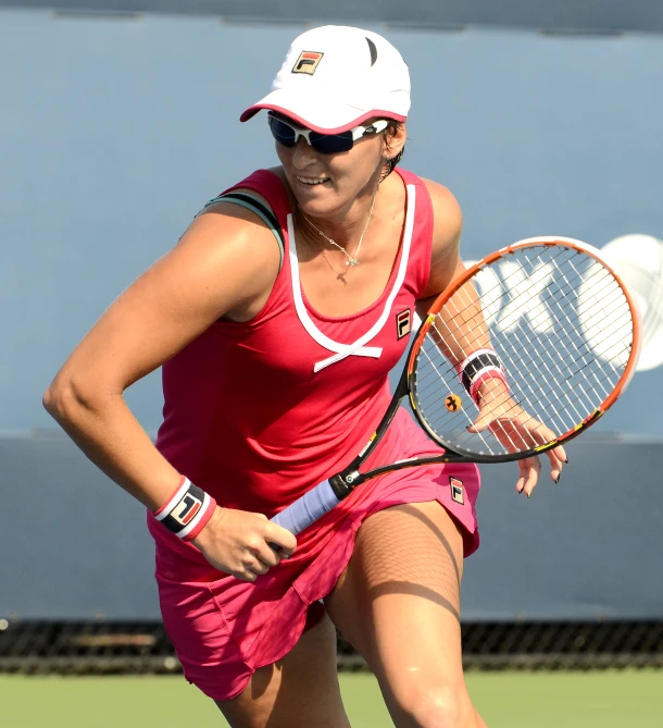 a woman in a red shirt and white hat holding a tennis racquet