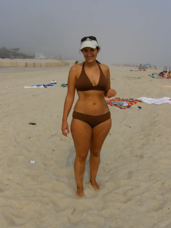 a woman wearing a brown bikini and white hat standing on the beach