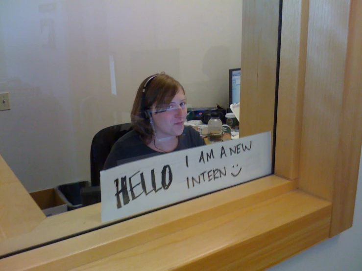 woman with headphones sits behind a sign that reads, i am a new intern