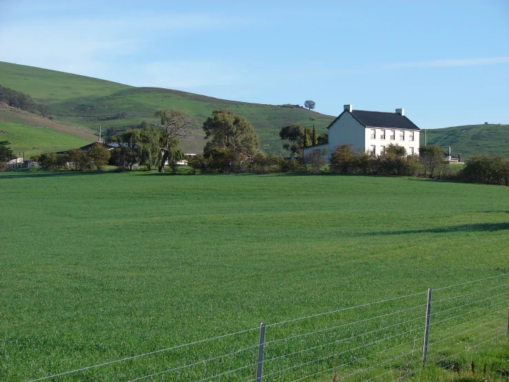 the house stands on a hill above a field of grass