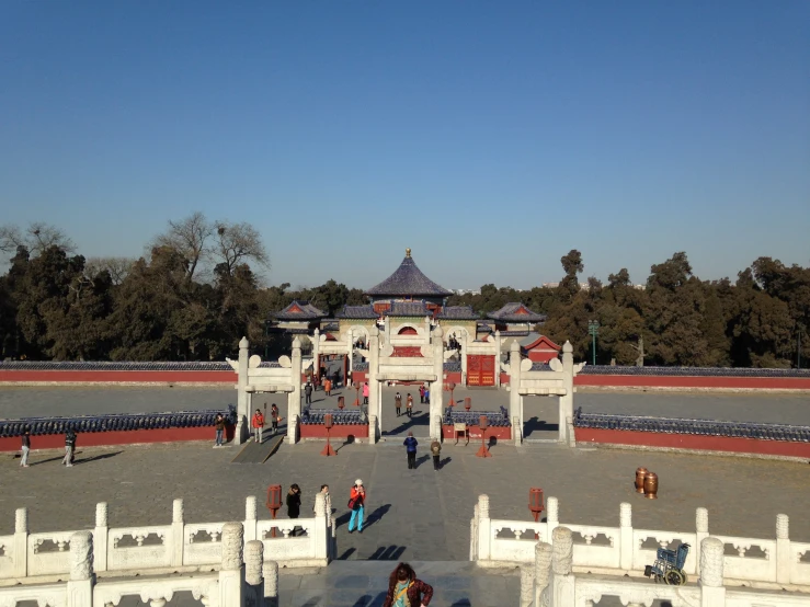 a white gate with an entrance to a large building and several people walking around