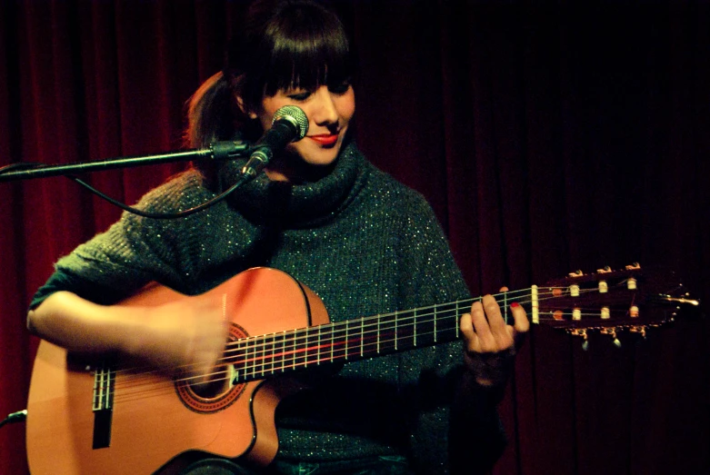 a woman is singing into a microphone while playing an acoustic guitar