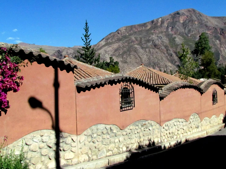 an adobe house sits by some mountains and flowers