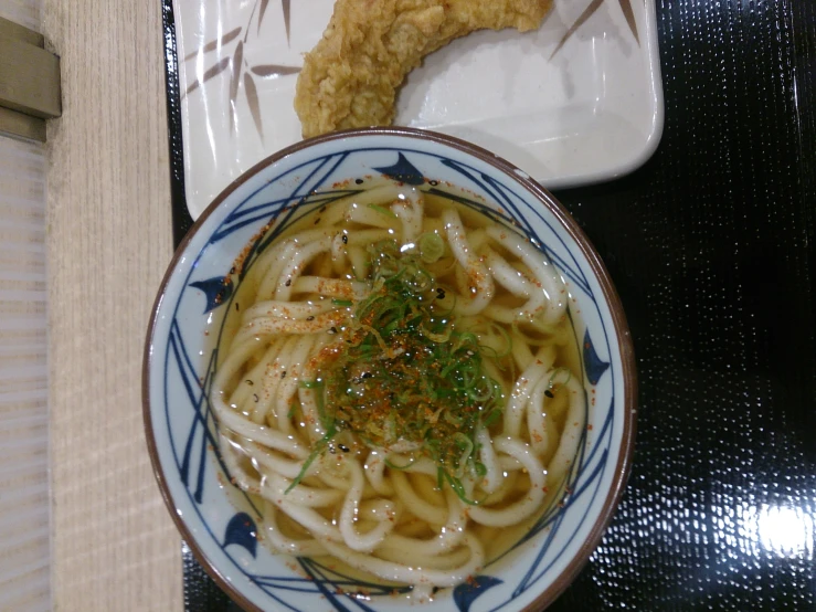 a plate with noodles and fried food beside a bowl of meat on a plate