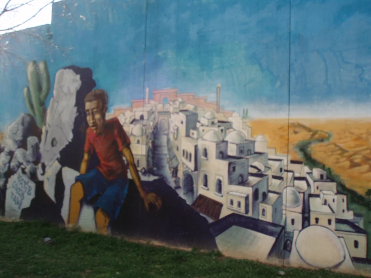 a painting on the side of a building depicts a man sitting in a canyon, with buildings all around