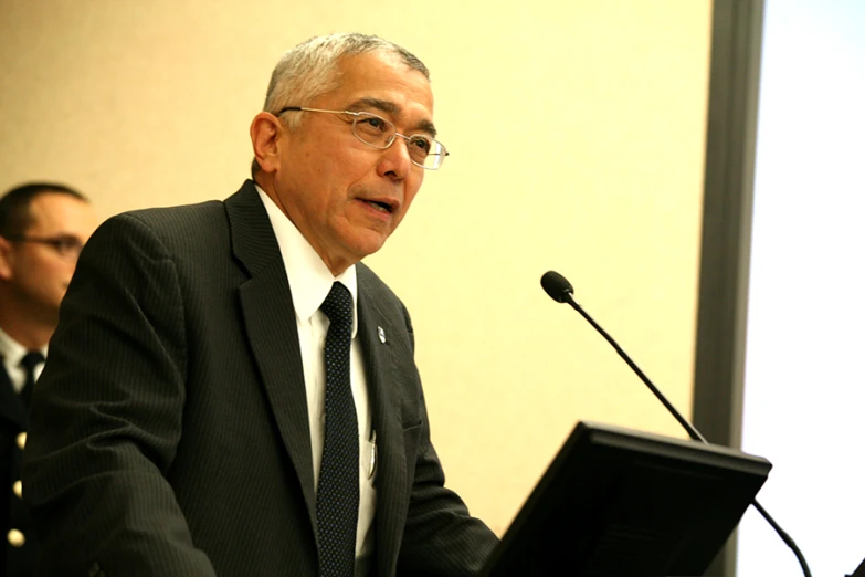 a man in a suit sitting at a desk with a microphone