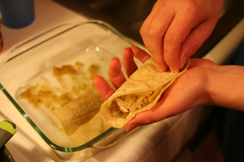 hands are reaching out for tortilla with sauce in glass dish