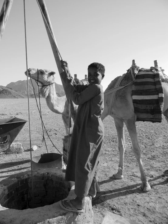 a man holding a piece of machinery and standing next to two camels