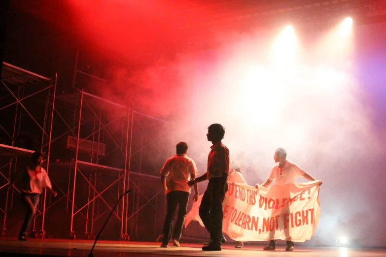 three people in dark and stage lighting holding an umbrella