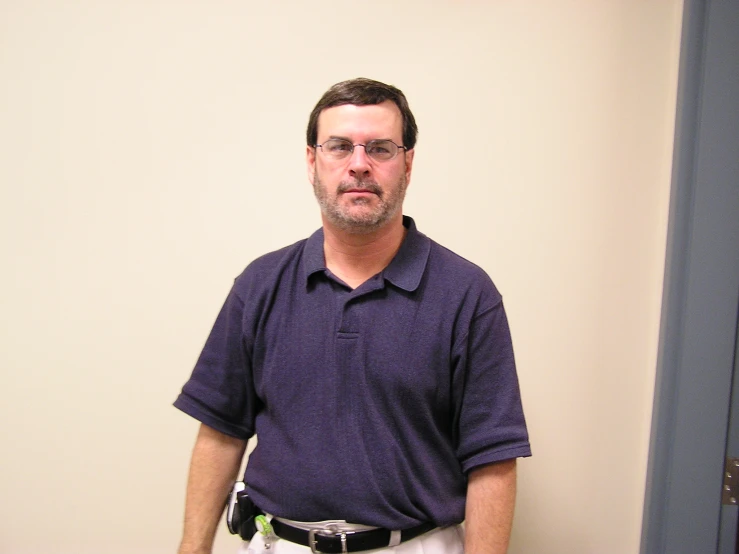 a man stands in front of a white wall wearing a black belt and wearing a purple shirt