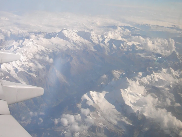 the view from the window on an airplane flying in the sky above mountains