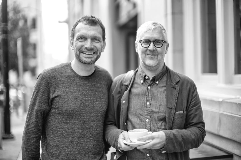 two men posing for the camera holding coffee cups