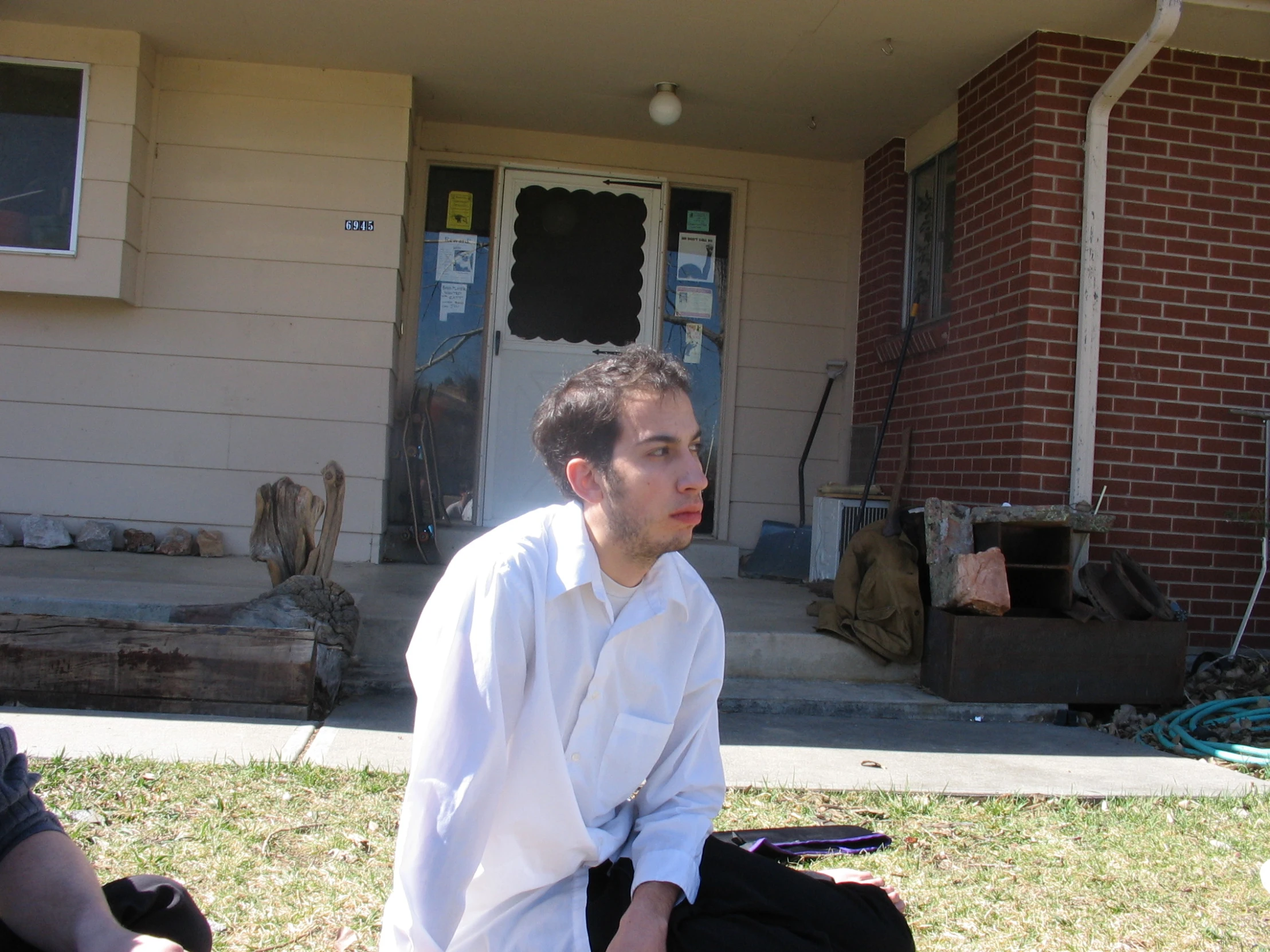 a young man sits outside a house wearing white