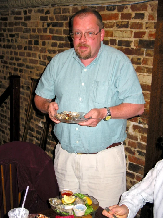 a man in a blue shirt and glasses holding a plate with food