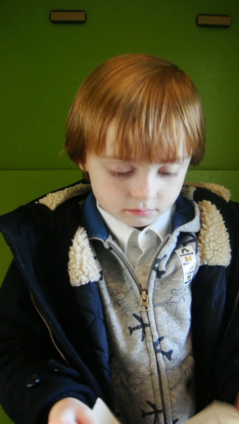 boy reading a book in front of green wall