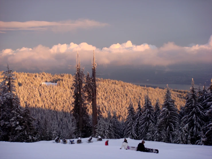 two people sitting on snow covered ground with trees in the background