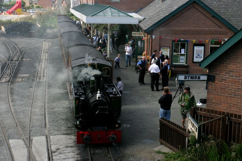 people standing on a platform and watching a steam train going down the track