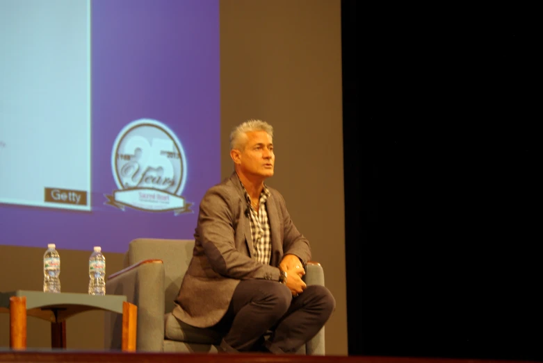 a man sits on a chair while speaking to a group