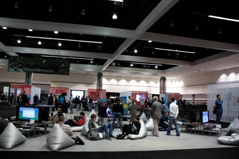 a large group of people are sitting and standing at the exhibition