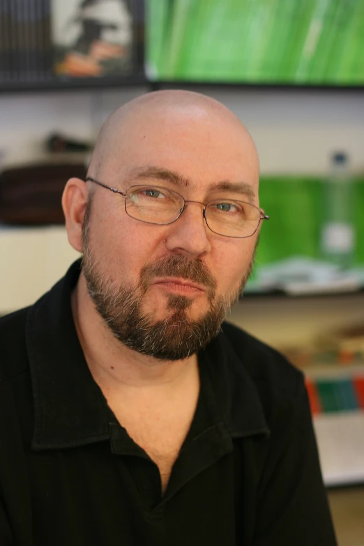a bald man wearing glasses stares intently at the camera