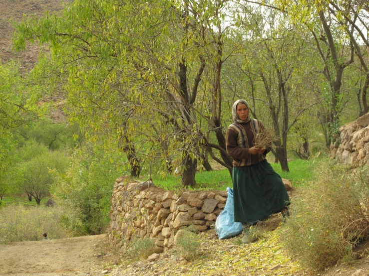 the lady is standing outside by a stone wall