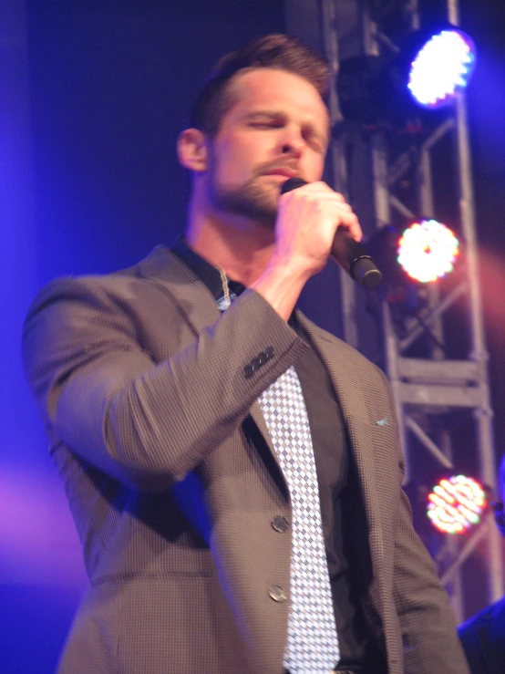 a male in a gray suit a microphone and lights