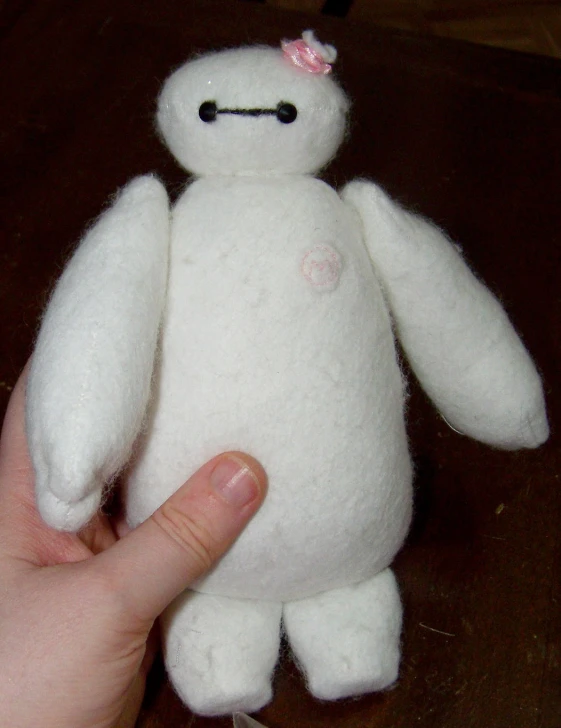 a hand holding a white stuffed bear on a wooden table