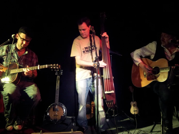 three men are playing music and guitar in the dark