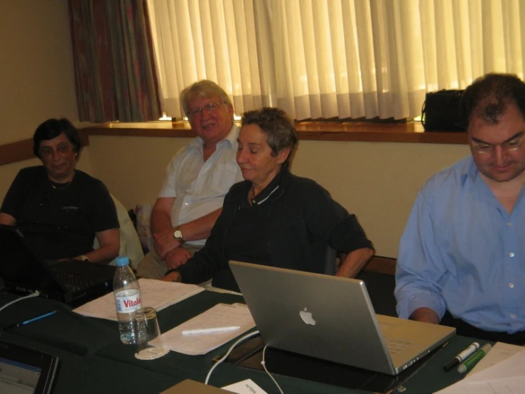 four men and two women sitting in front of a laptop