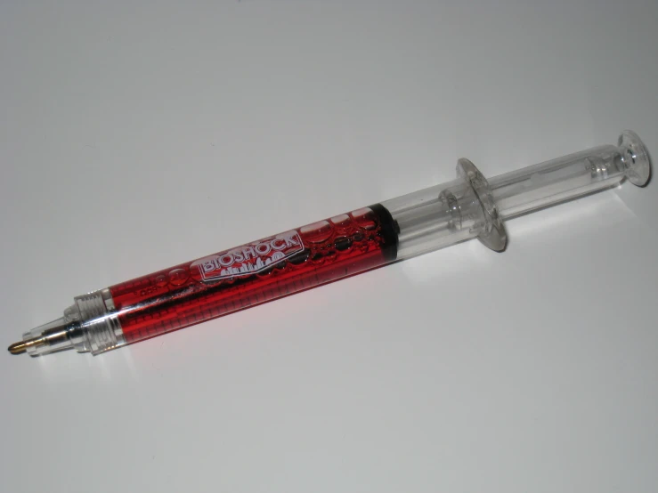 a red pen with clear plastic tip lying on top of a table