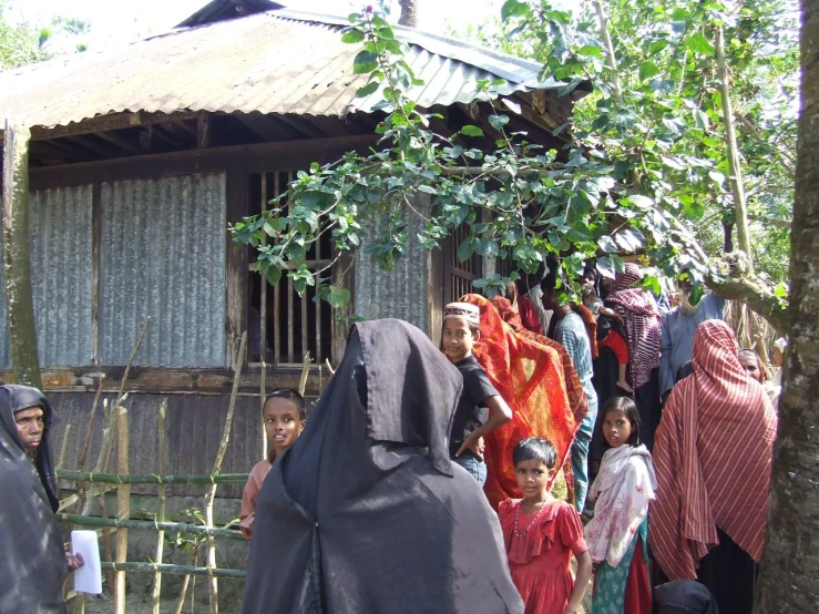 women in traditional garb are standing around a small hut