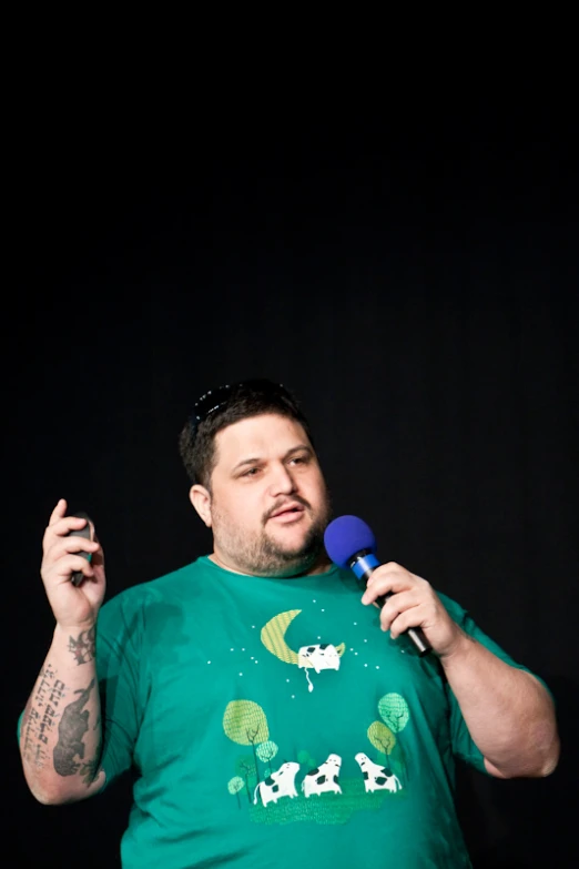 man with tattoos wearing green t - shirt and holding microphone