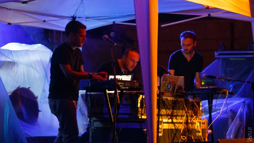 three men working on their electronic devices in a tent