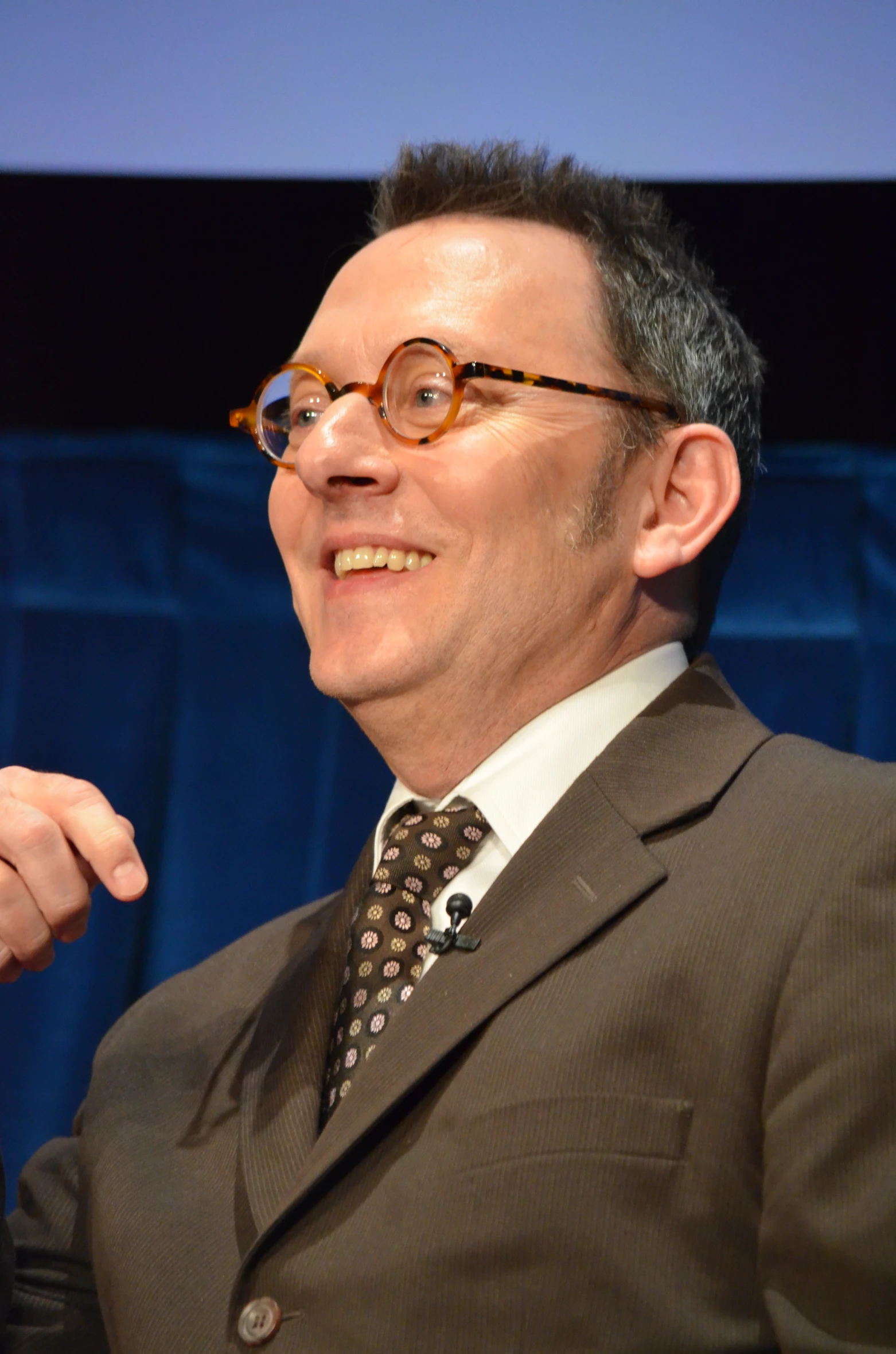 man wearing glasses and suit in front of a projection screen