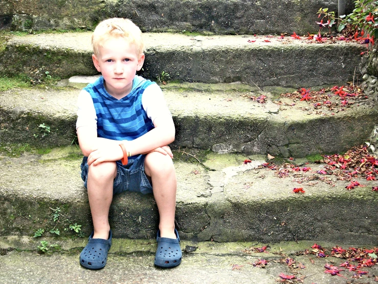 a little boy sitting on some steps with his hands folded