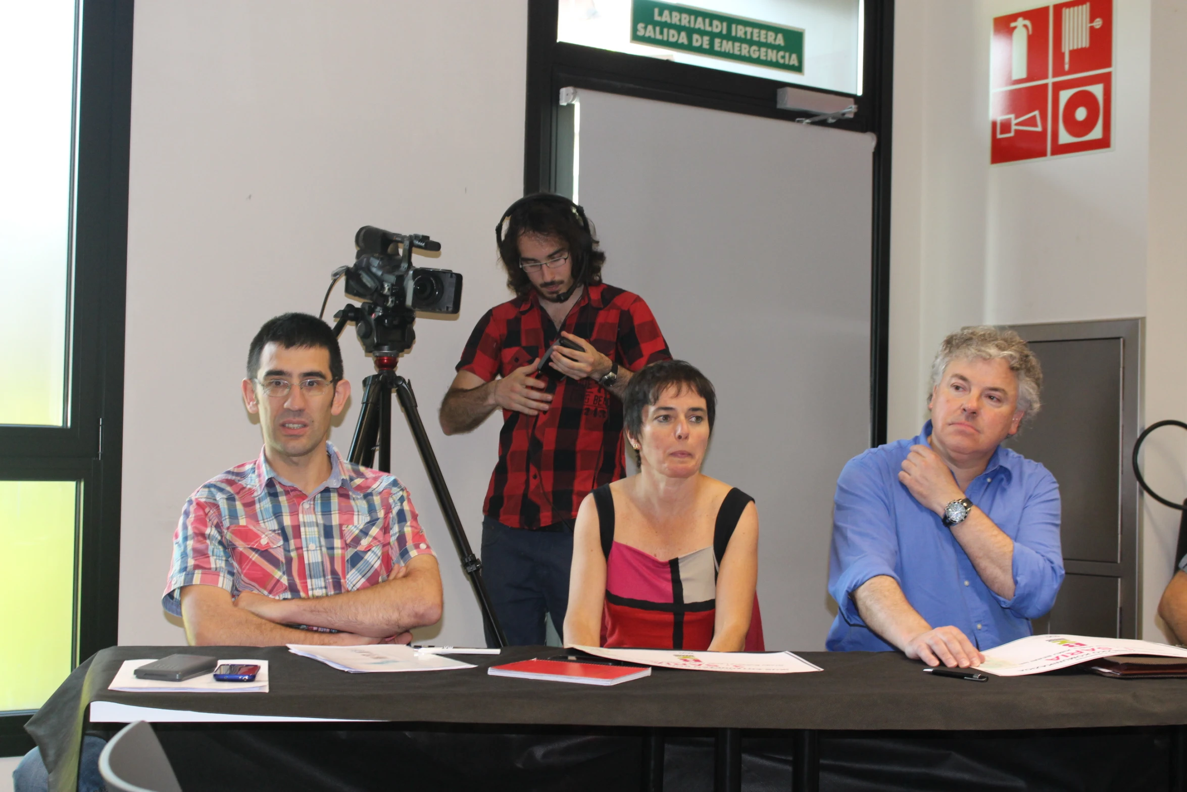 four people sitting at a table while two microphone stands nearby