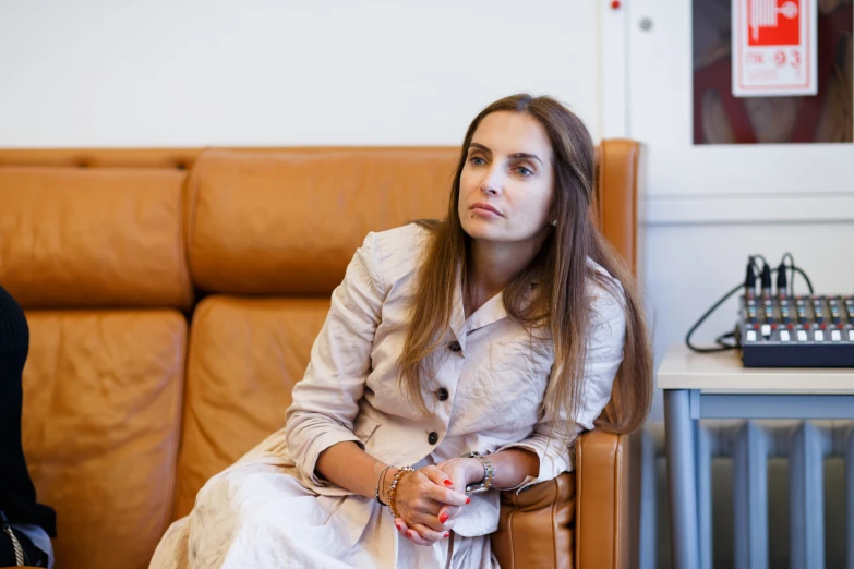 a woman sits on a brown leather chair next to a wall