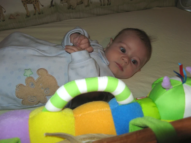 a little baby lays on a bed next to toys